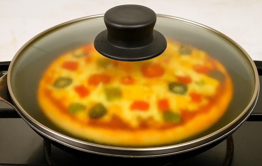 तवे पर प्लेट समेत पिज़्ज़ा को ढक्कन लगाकर मीडियम आंच पर पकाया जा रहा है