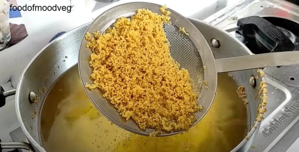 गरम तेल में जीरो साइज छलनी से बेसन घोल डालकर बूंदी तलते हुए