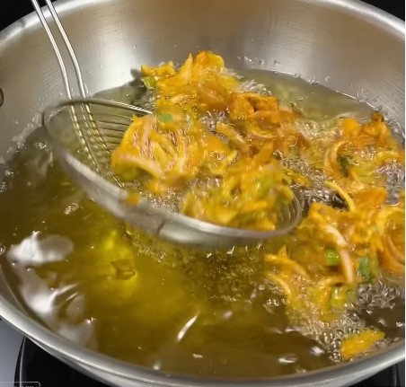 गर्म रिफाइंड तेल वाली कड़ाही में हाथ से थोड़ा-थोड़ा पकौड़ी मिक्स डालते हुए तला जा रहा है।