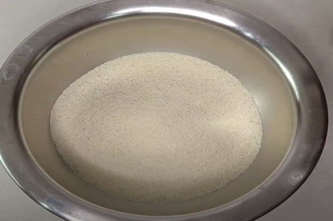 कटोरी में सूजी को छानते हुए – स्मूद इडली बैटर के लिए छानी हुई सूजी का इस्तेमाल