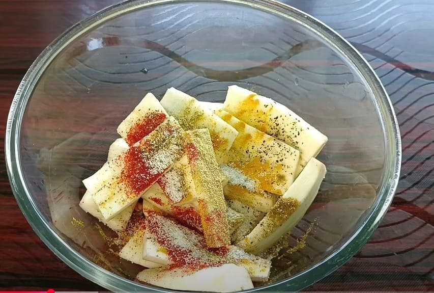 कच्चे केले के टुकड़ों को हल्दी, मिर्च और मसालों में मेरिनेट करते हुए – पकाने से पहले का स्टेप