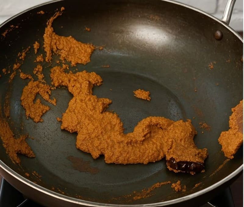 लोहे की कड़ाही में मेथी, सूखी मिर्च और प्याज़-लहसुन प्यूरी के साथ मसाले भूनते हुए