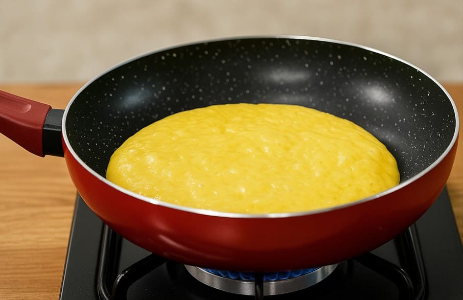 नॉनस्टिक पैन में बेसन और मावा का घोल गोल शेप में फैलाकर धीमी आंच पर पकाते हुए