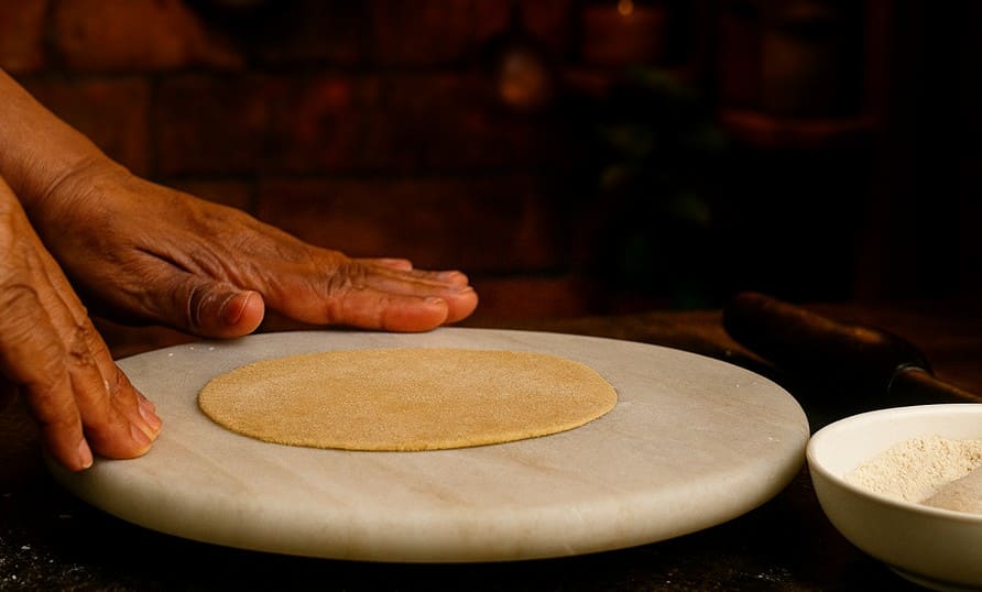 भटूरे की लोई को सूखे आटे में डुबोकर बेलन से लंबा आकार बेलते हुए – तले के लिए तैयार किया जा रहा है