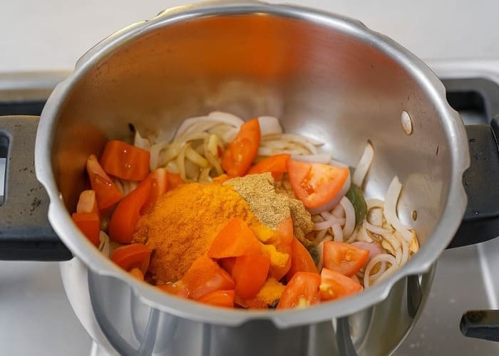 कुकर में सरसों का तेल, प्याज, मसाले और अदरक-लहसुन पेस्ट को भूनते हुए